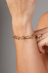 A gold chain bracelet with textured links and small bead accents, shown worn on a person&