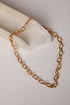 A gold-toned chain necklace with elongated oval links, draped over a white fabric-covered display stand on a light neutral background.