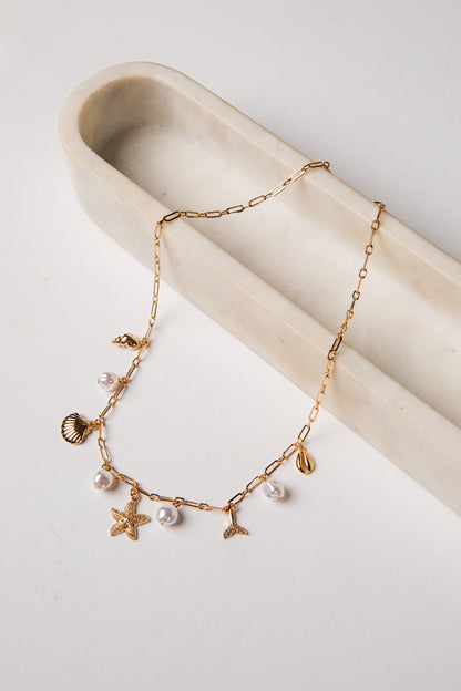 Gold necklace with starfish, shell, and pearl charms on a white surface.