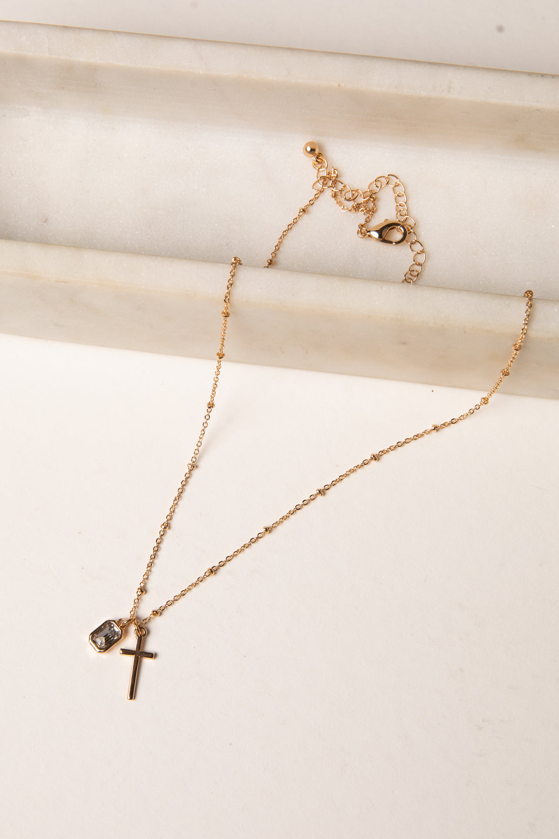 Gold necklace with a cross pendant on a light wooden surface
