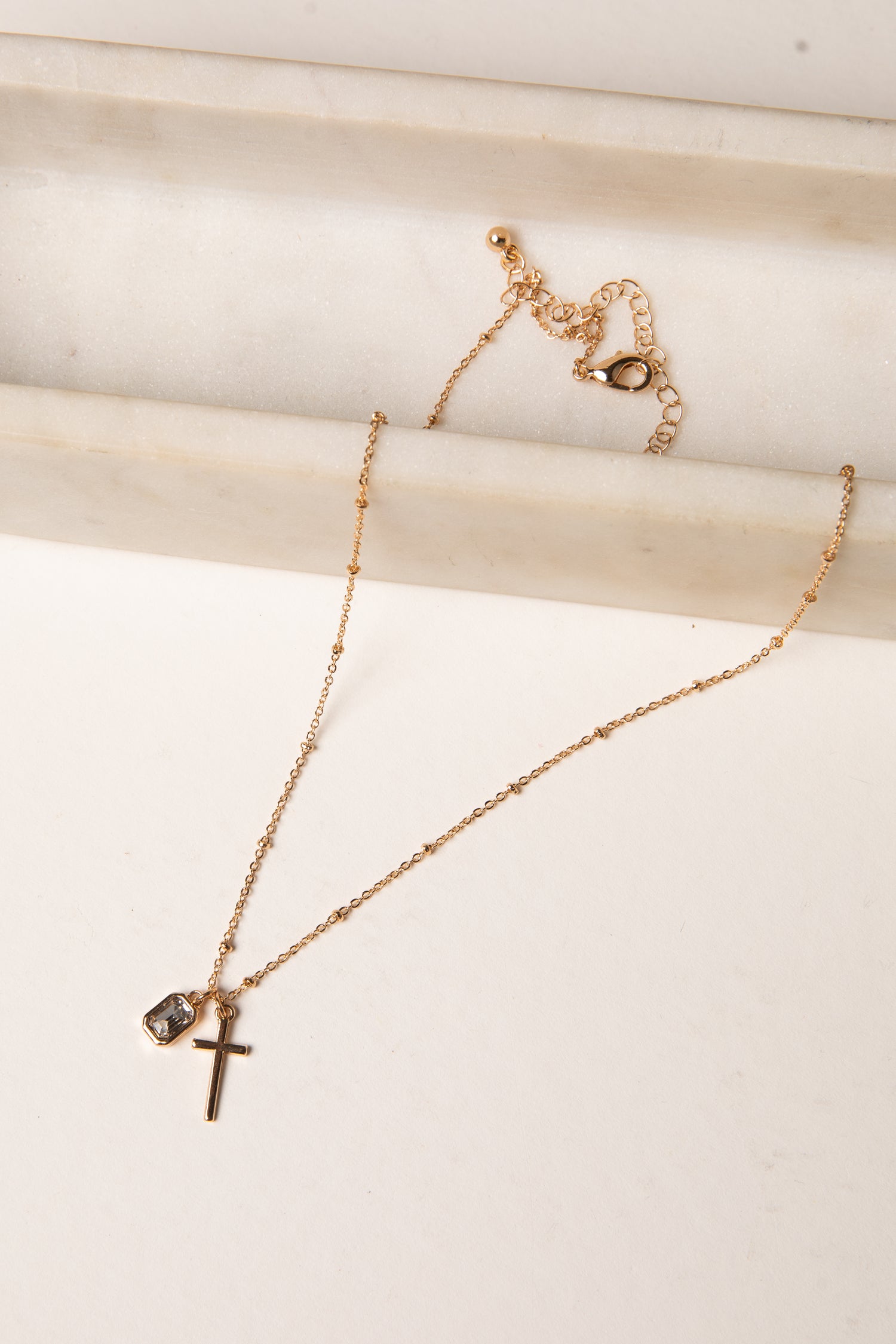 Gold necklace with a cross pendant on a light wooden surface