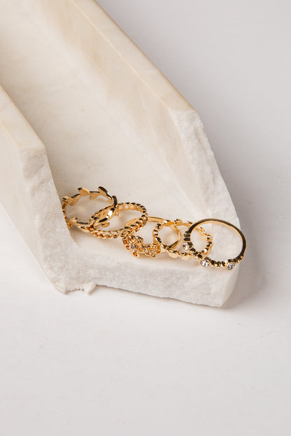 A set of gold-toned textured rings arranged on a white textured stone tray against a clean white background.