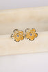 Gold flower-shaped earrings with a central gemstone on a beige cushion.
