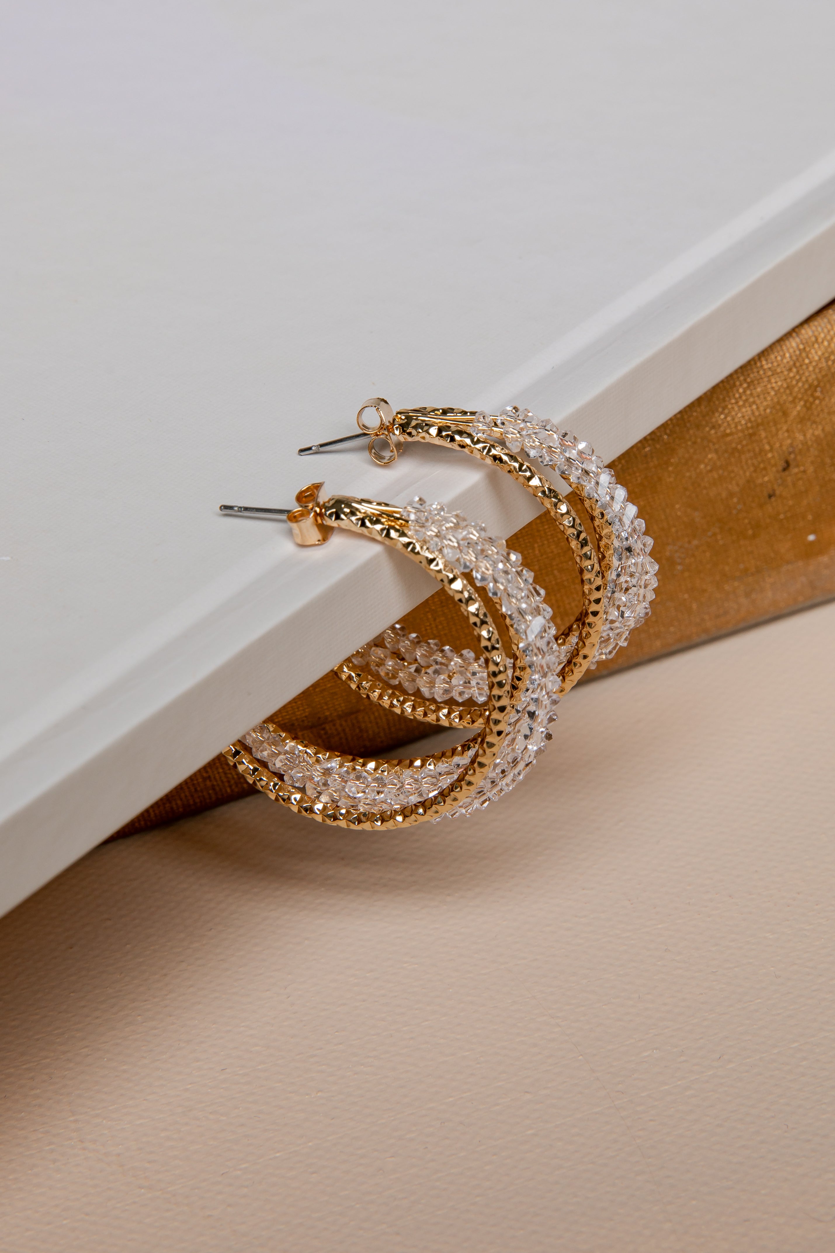 Gold hoop earrings with clear gemstones on a beige surface