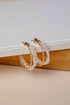 Pair of gold and pearl hoop earrings on a textured surface with a neutral background