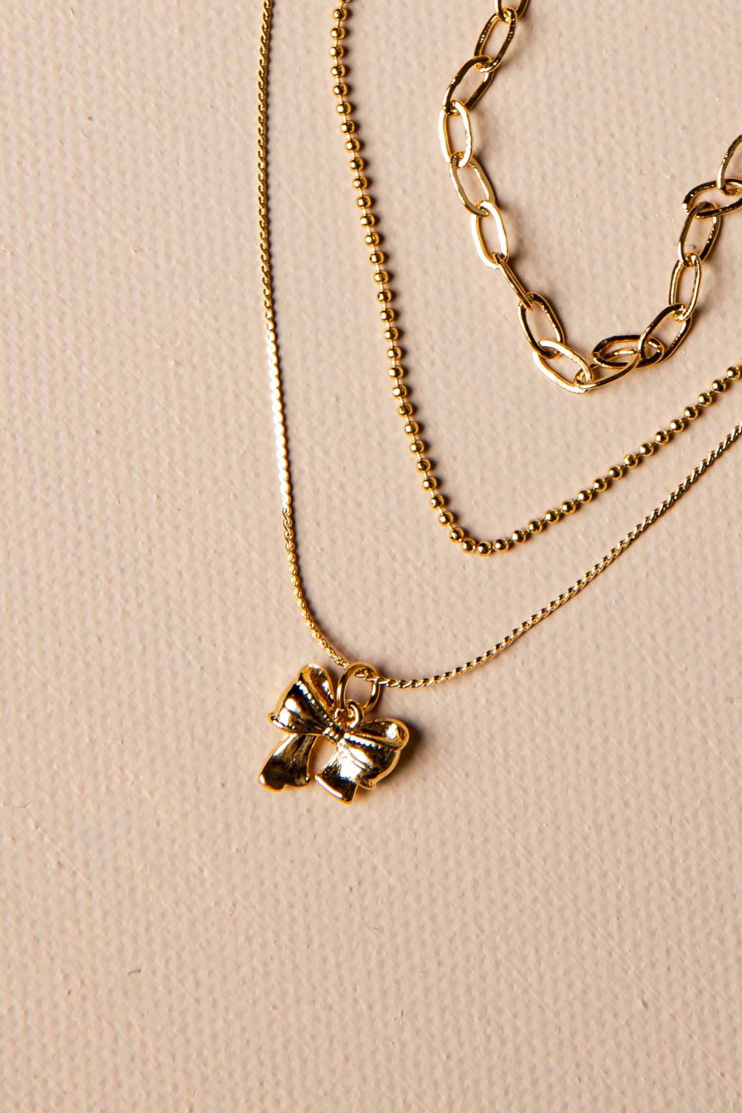 Three gold necklaces with different designs on a beige background