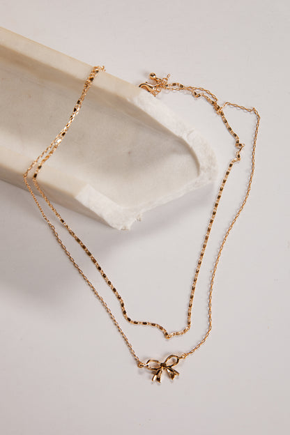 Gold necklace with a bow pendant on a light background
