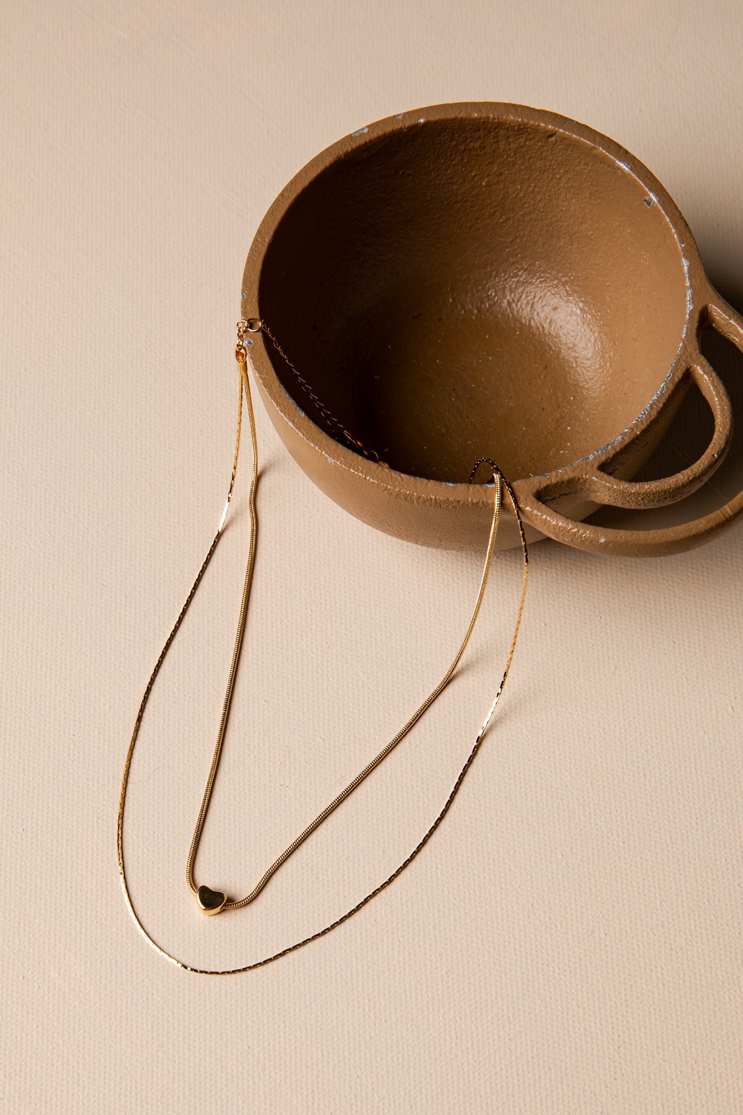 Brown ceramic bowl with a gold necklace on a beige background