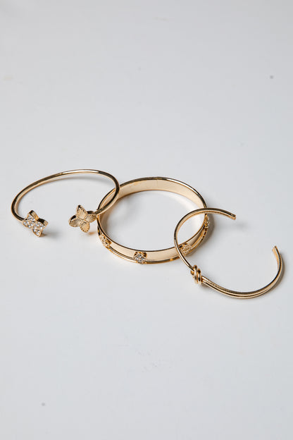 Three gold bracelets with decorative elements on a light gray background
