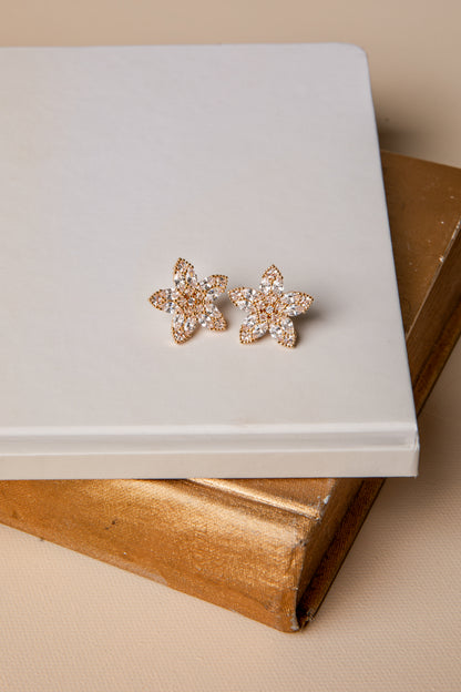 Pair of floral earrings on a white surface with a beige background