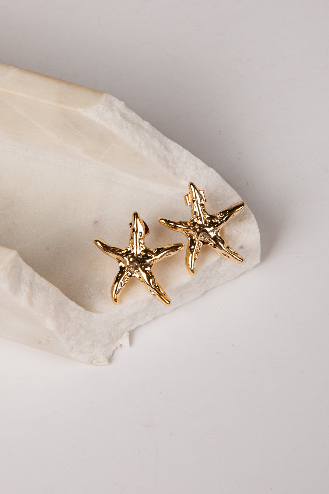 Gold starfish earrings on a white stone surface