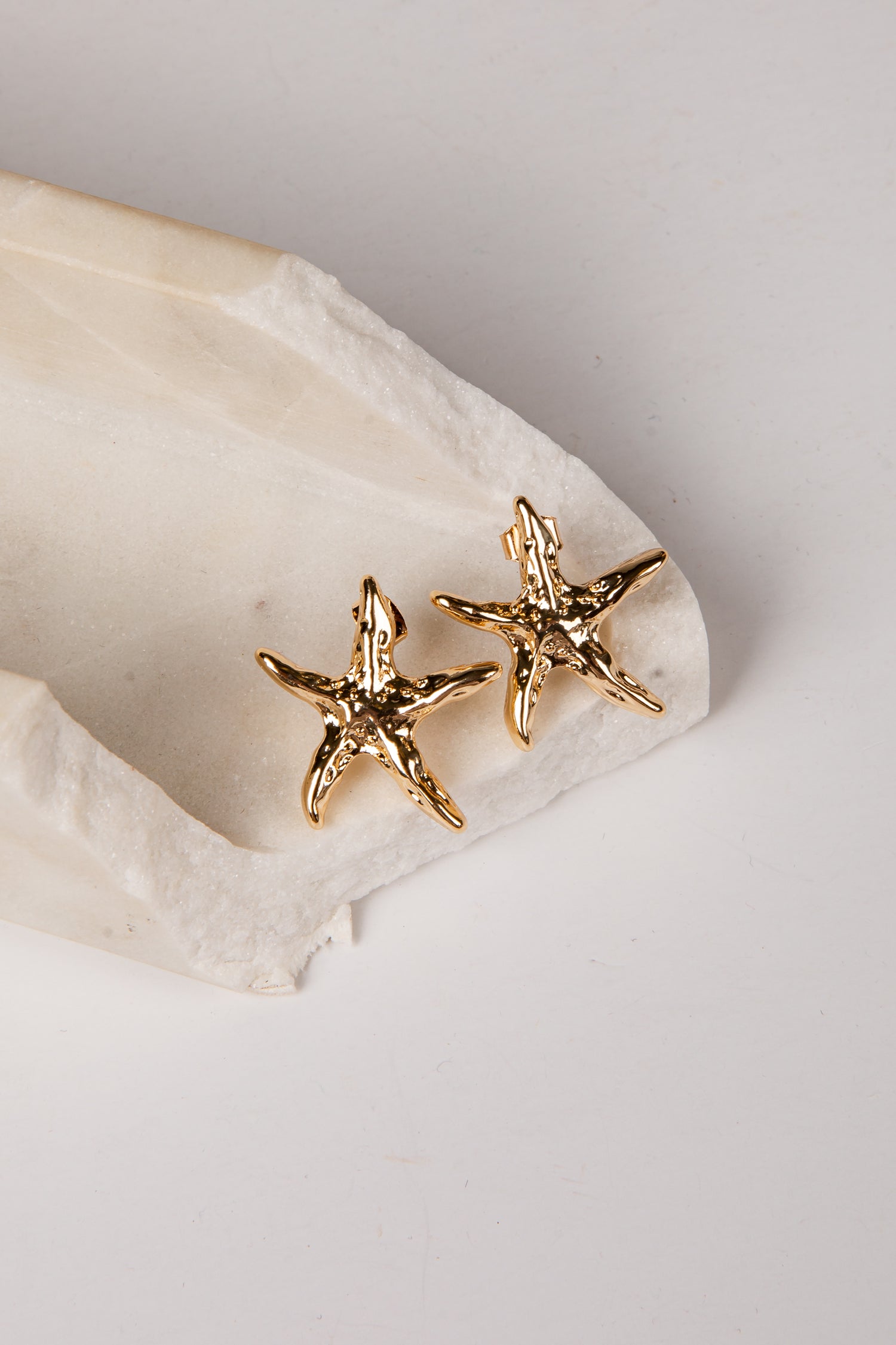 Gold starfish earrings on a white stone surface