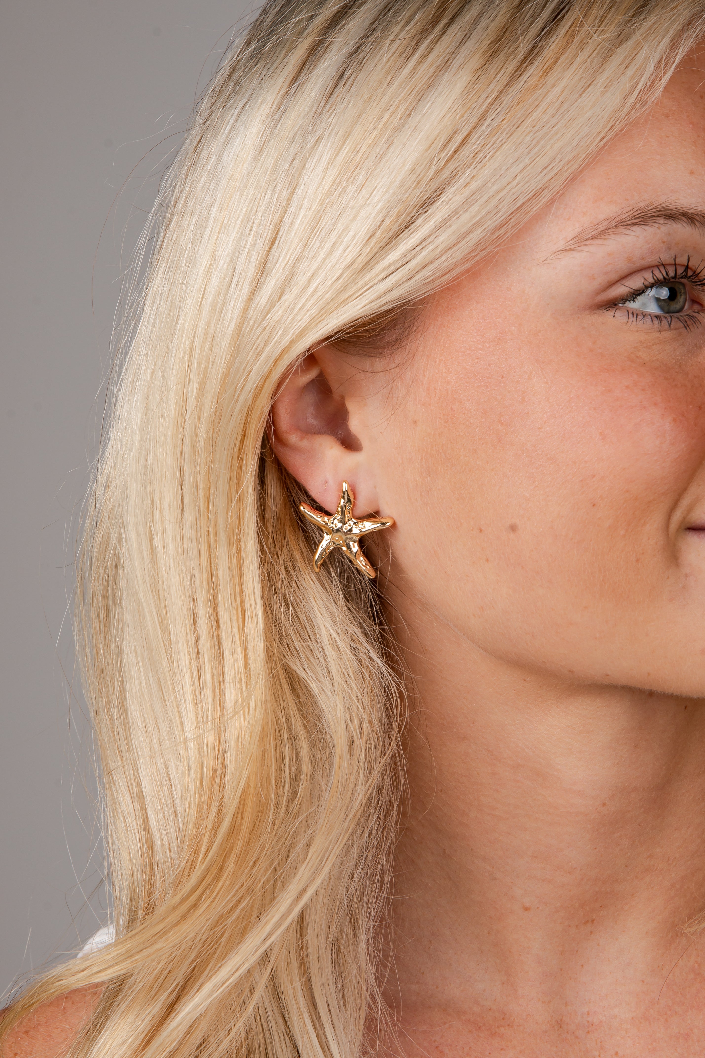 Close-up of a woman wearing a gold star-shaped earring against a neutral background