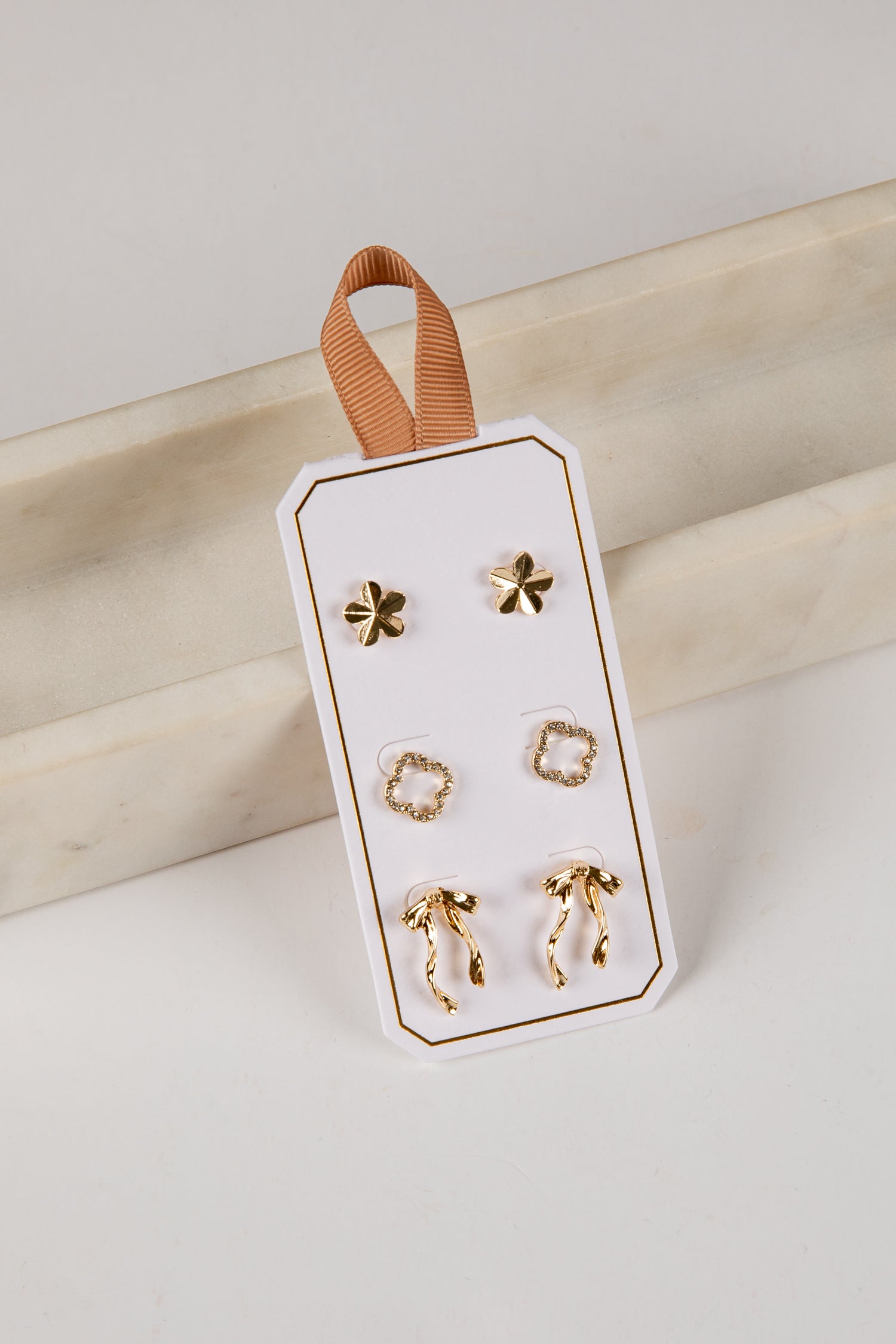 Set of gold earrings on a white card with a brown ribbon against a light background