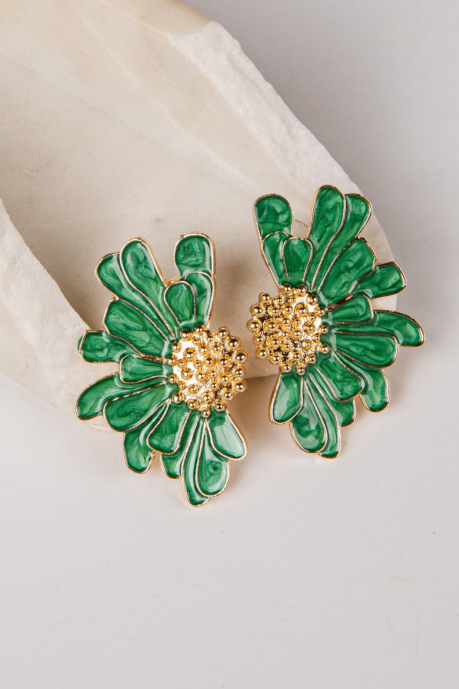 Green floral earrings with gold centers on a white fabric background
