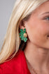 Close-up of a woman wearing green floral earrings with a red top and gray background