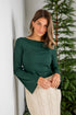 Woman wearing a green top and white skirt standing next to a Christmas tree.