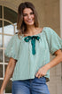 Woman wearing a green and white striped blouse with a bow tie, standing outdoors.
