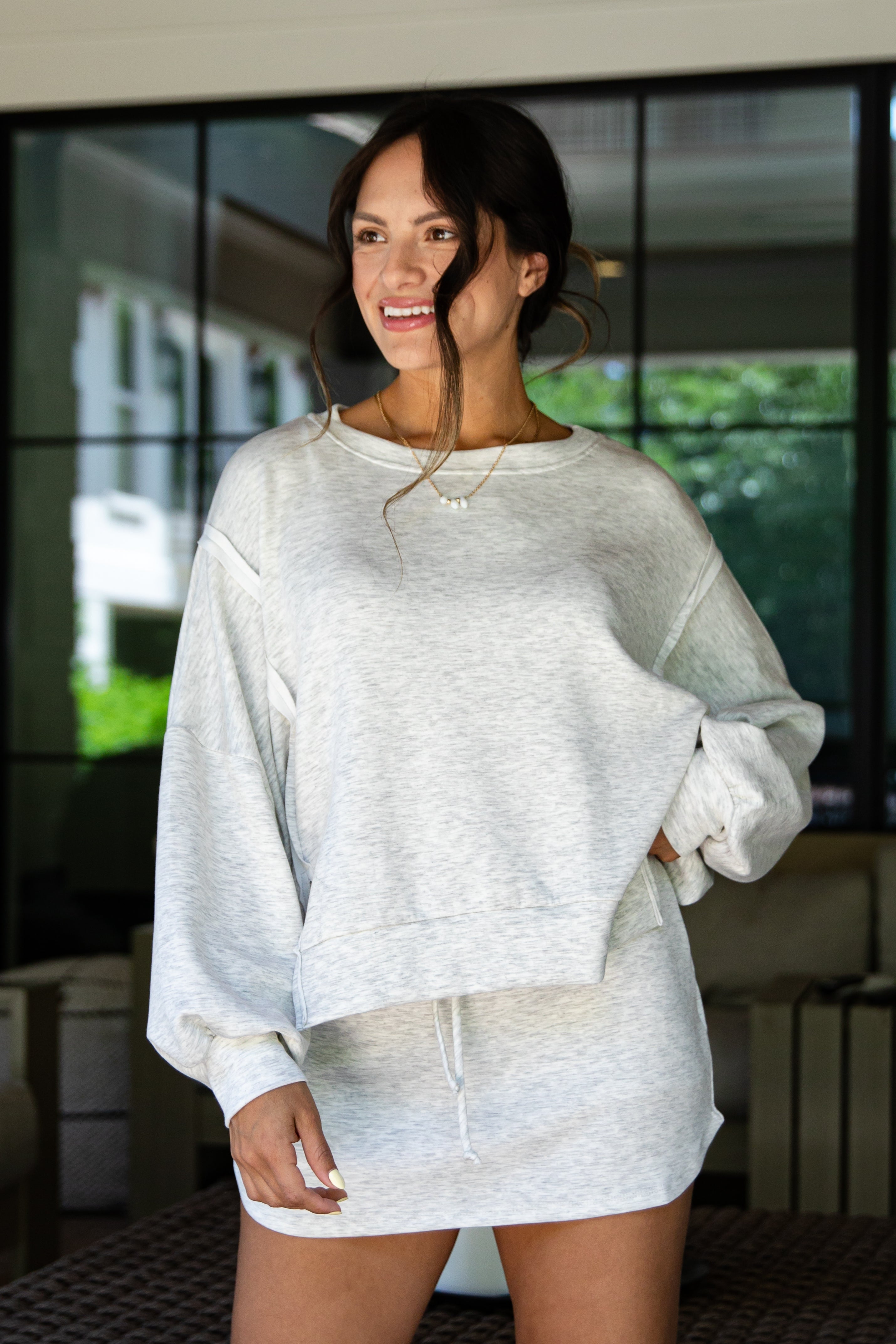 Woman wearing a light gray sweater and skirt set in an outdoor setting.