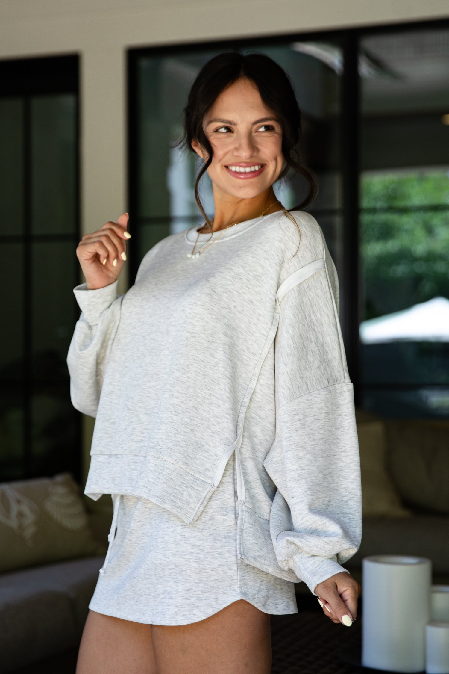Woman wearing a light gray sweatshirt and shorts in an indoor setting.