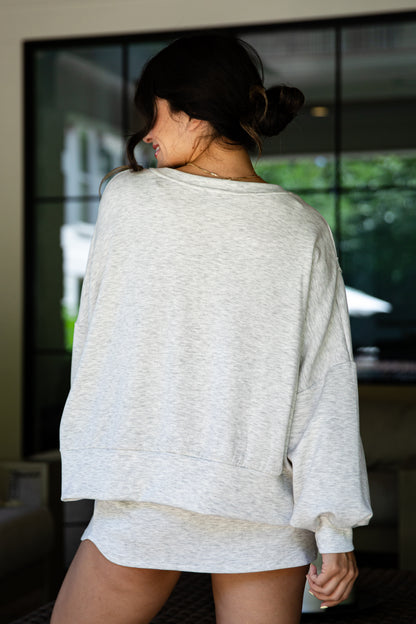Woman wearing a grey oversized sweatshirt in an indoor setting