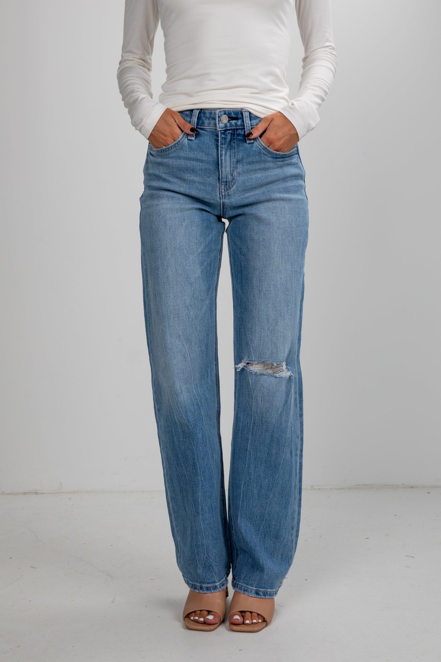 Person wearing light blue jeans and a white long-sleeve shirt on a plain background