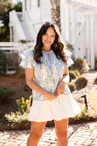 Woman in a floral top and white skirt standing outdoors with a white house in the background
