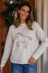 Woman wearing a beige sweater with a graphic design, standing in front of a wooden door.