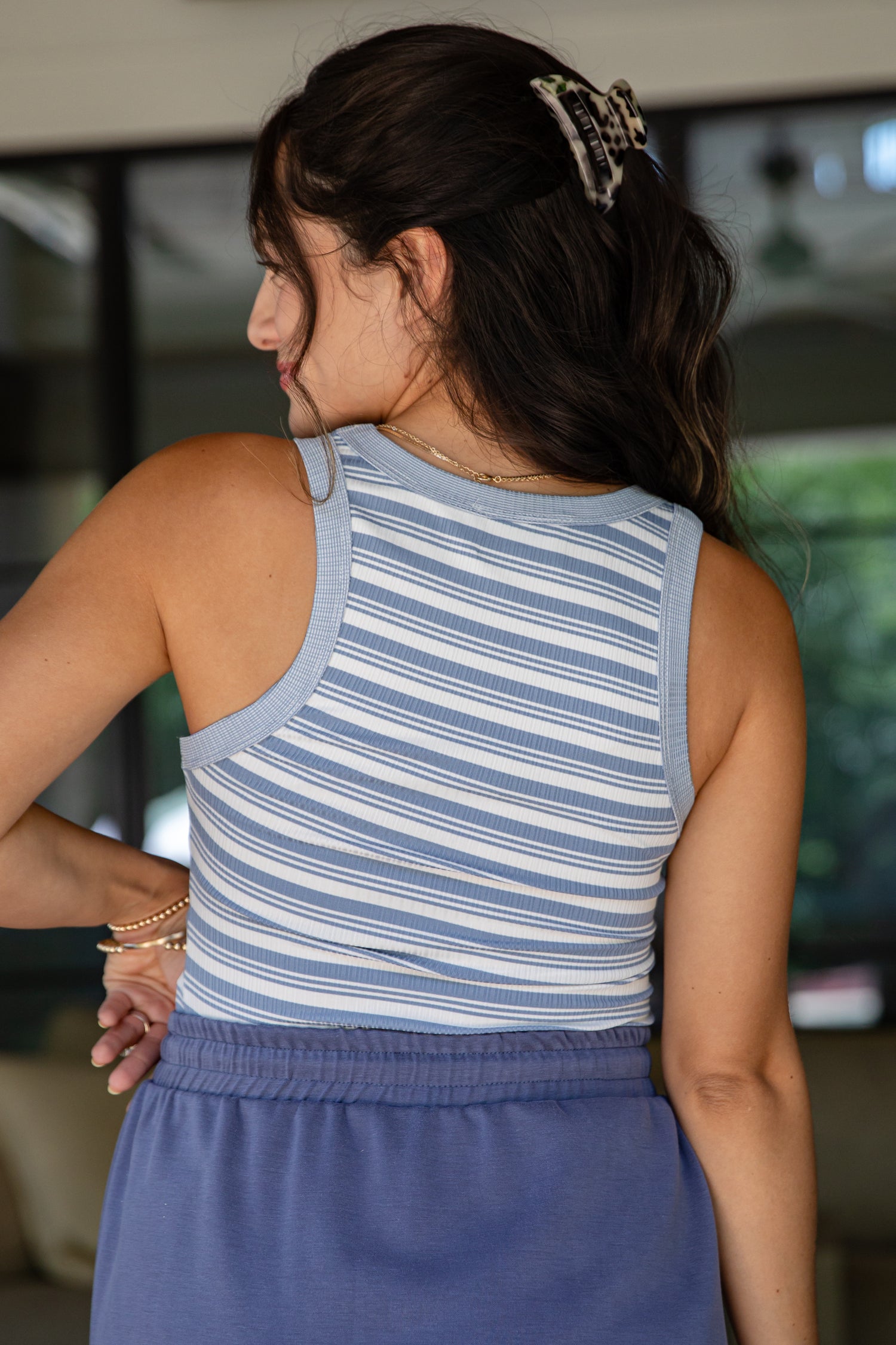 Woman wearing a blue and white striped sleeveless top and blue skirt, standing indoors.