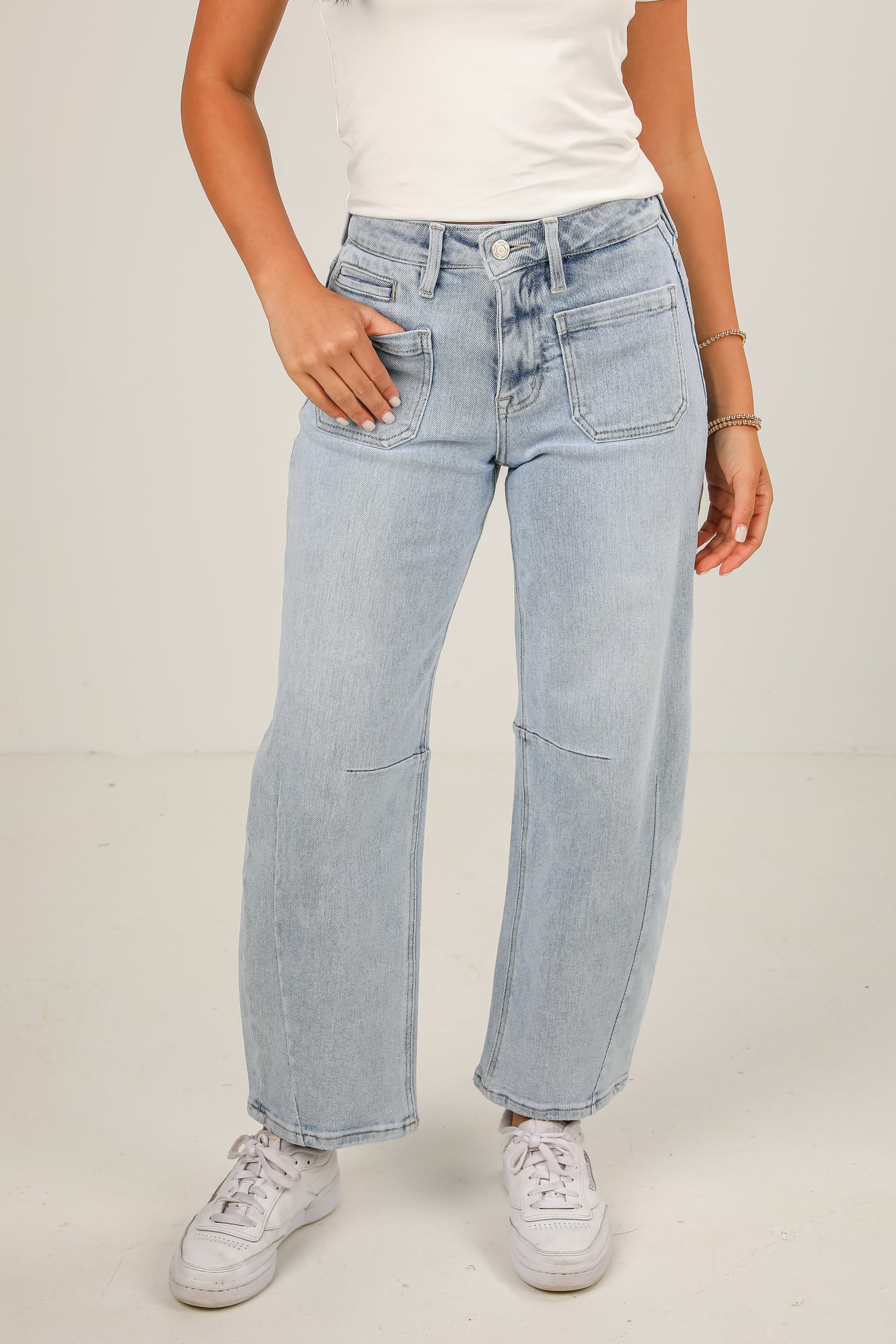 Person wearing light blue jeans and white sneakers on a plain background