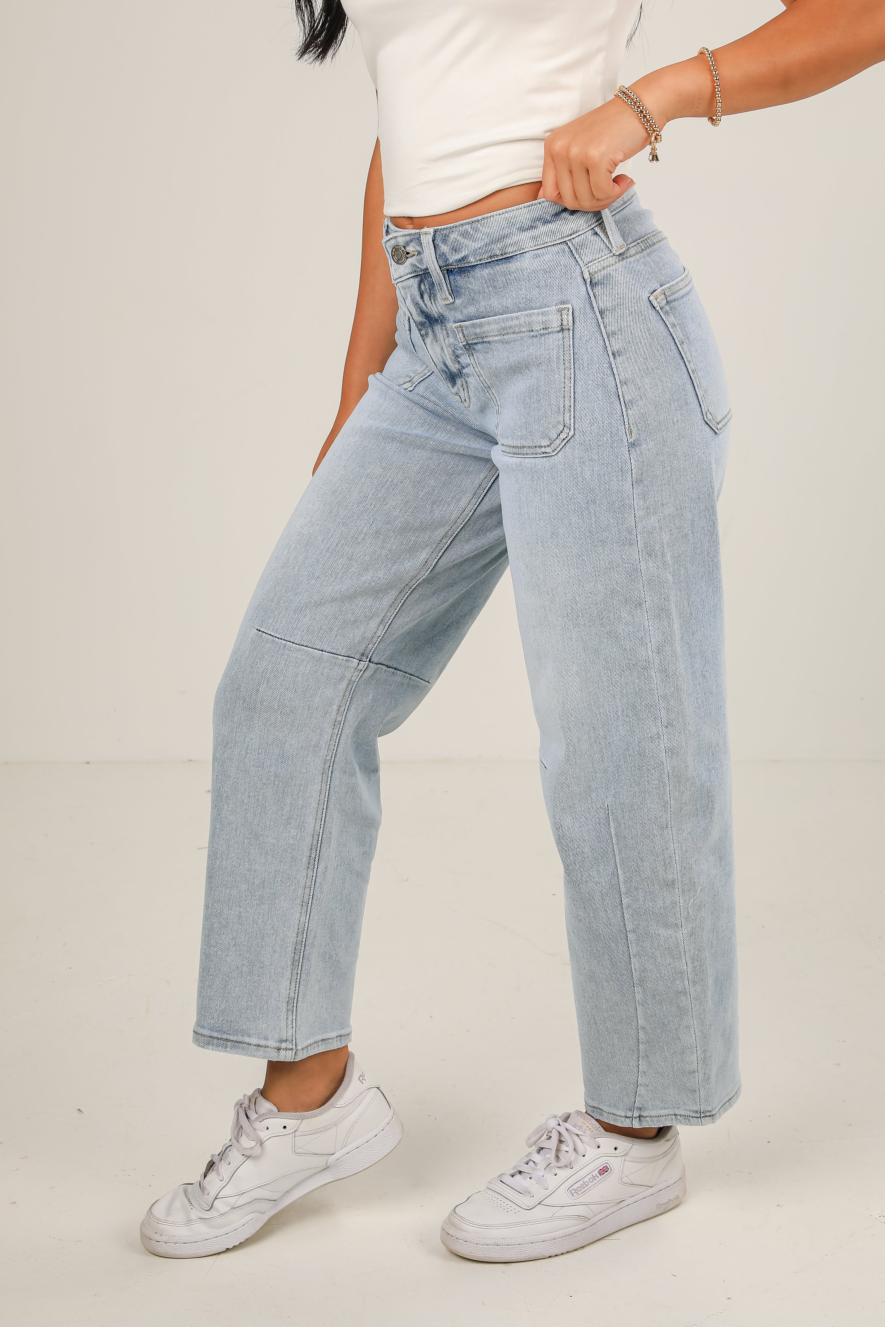 Person wearing light blue jeans and white sneakers on a plain background