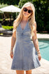 Woman in a denim dress standing by a pool with sunglasses on