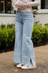 Person wearing light blue flared jeans standing outdoors with greenery in the background