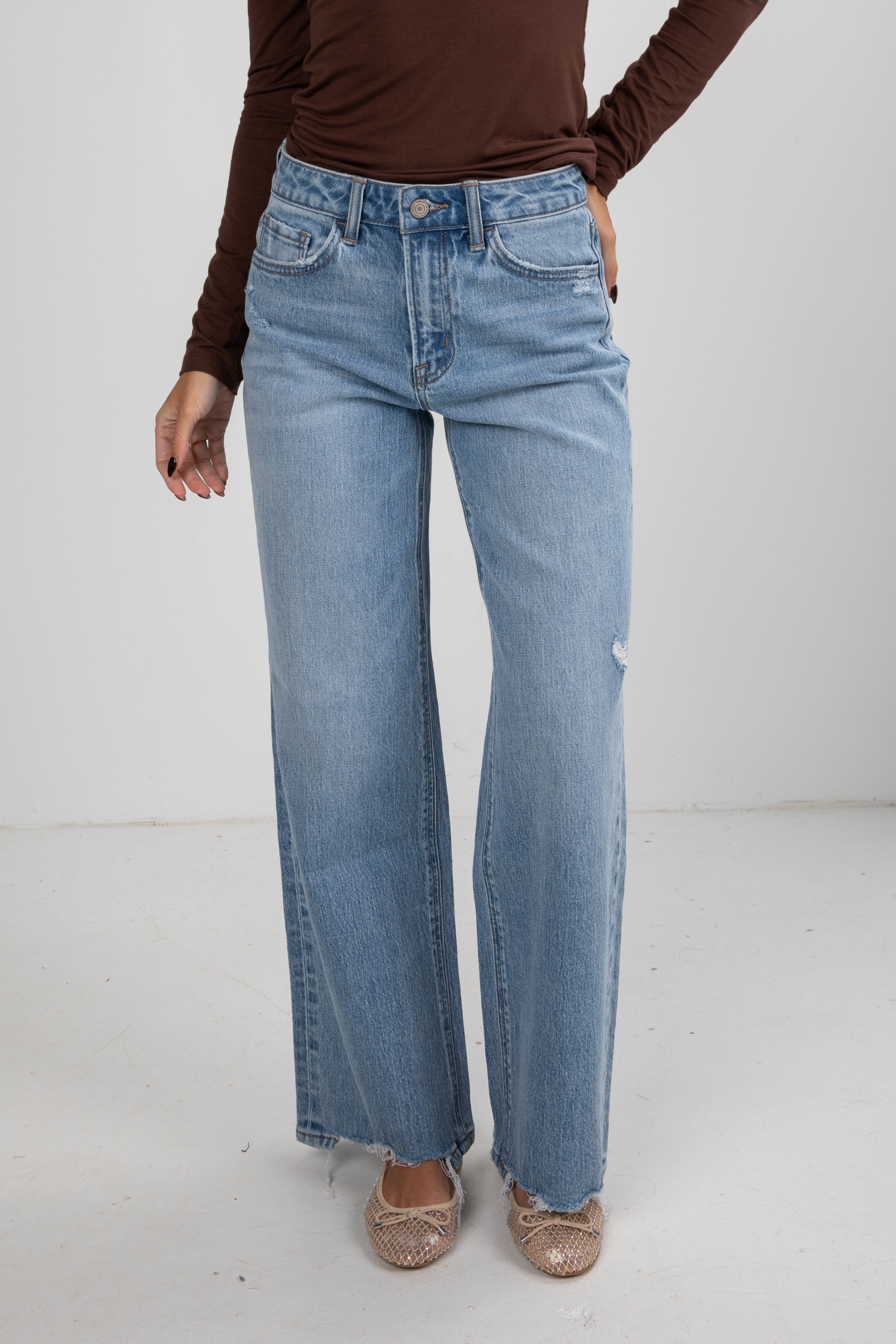 Person wearing light blue jeans and a brown top on a white background