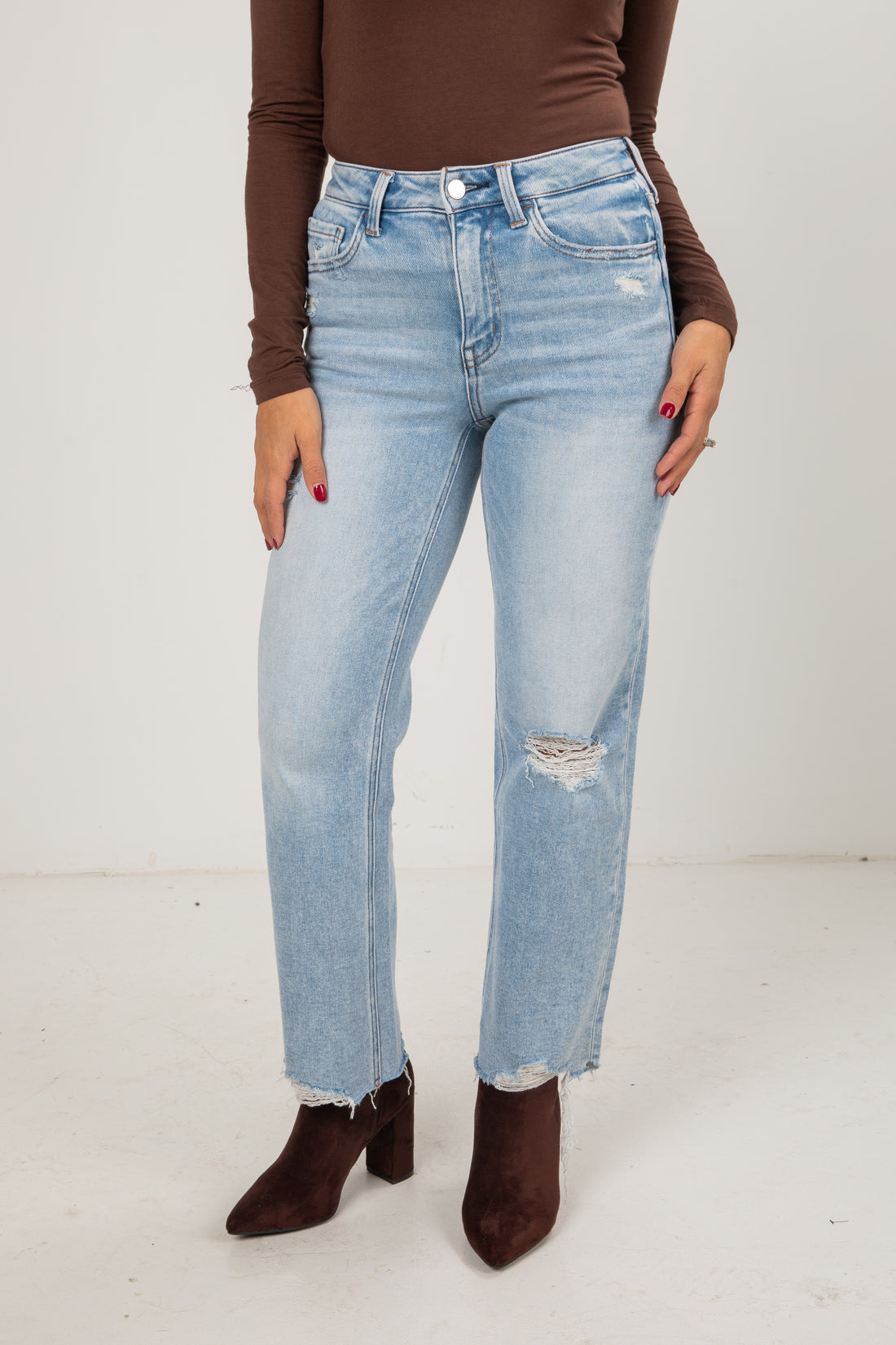 Person wearing light blue jeans and brown shoes on a white background