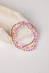 Three beaded stretch bracelets in pink and gold, displayed on a light beige textured stone prop against a white background.