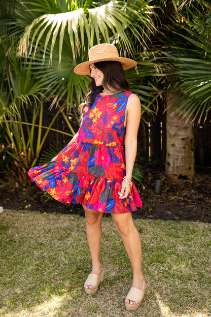 Woman in a colorful dress and hat standing in front of palm trees