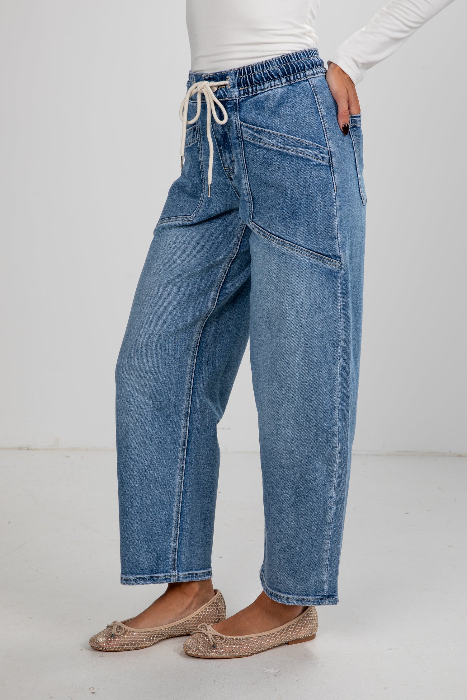 Person wearing blue jeans and beige flats on a white background