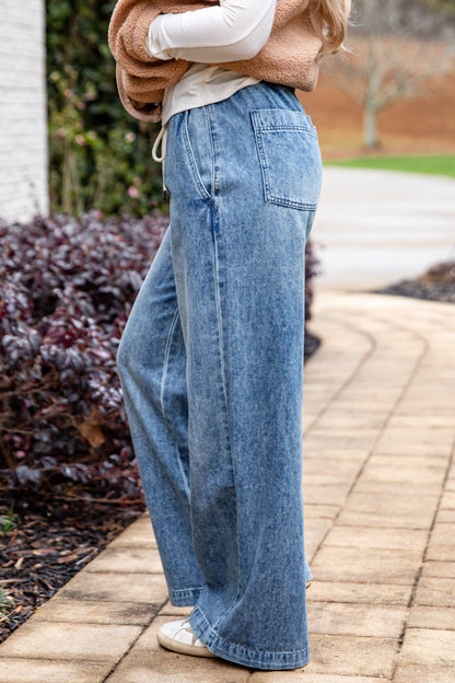 Person wearing blue jeans walking on a paved path with plants in the background