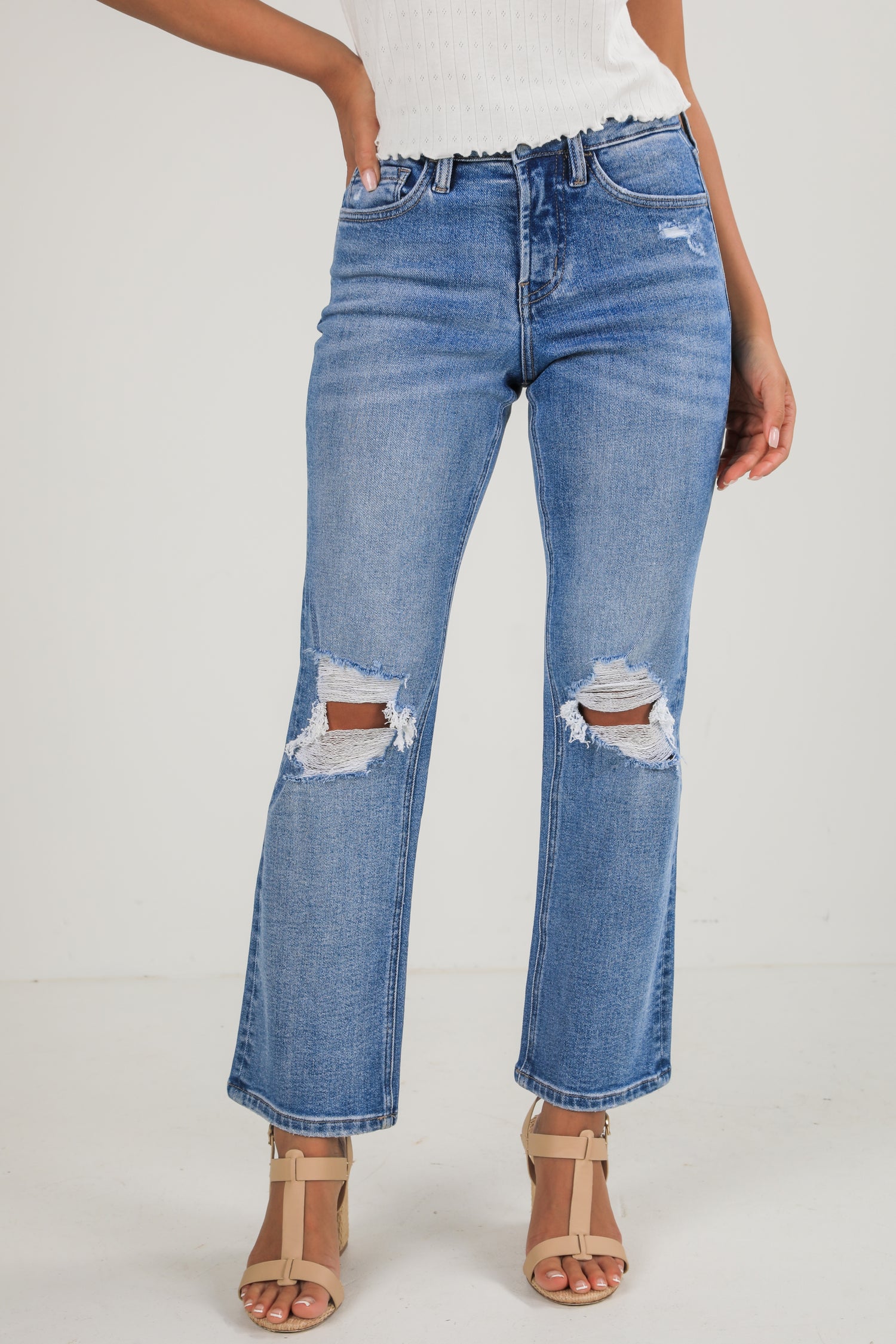 Person wearing distressed blue jeans on a white background