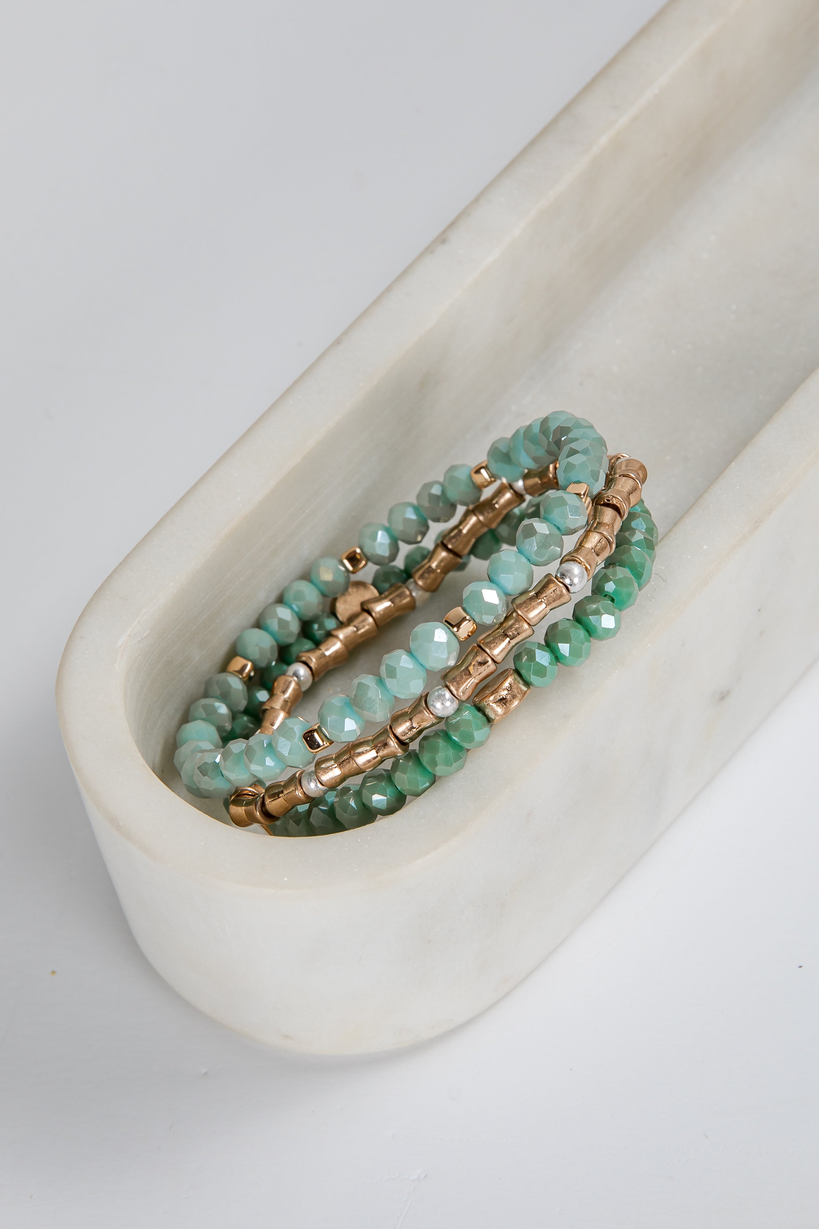 Set of green beaded bracelets on a white marble surface