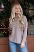 Woman wearing a beige sweater and blue jeans standing in front of a decorated Christmas tree.