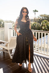 Woman in a black polka dot dress standing on a balcony with greenery in the background