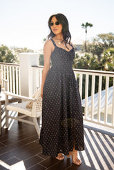 Woman in a black polka dot dress standing on a balcony with greenery in the background
