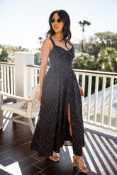 Woman in a black polka dot dress standing on a balcony with a scenic background.