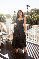 Woman in a black polka dot dress standing on a balcony with greenery in the background