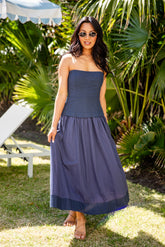 Woman in a navy strapless dress standing outdoors with greenery in the background