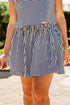 Woman wearing a navy and white striped short-sleeve top paired with a black-and-white striped mini skirt, standing outdoors by a pool on a sunny day