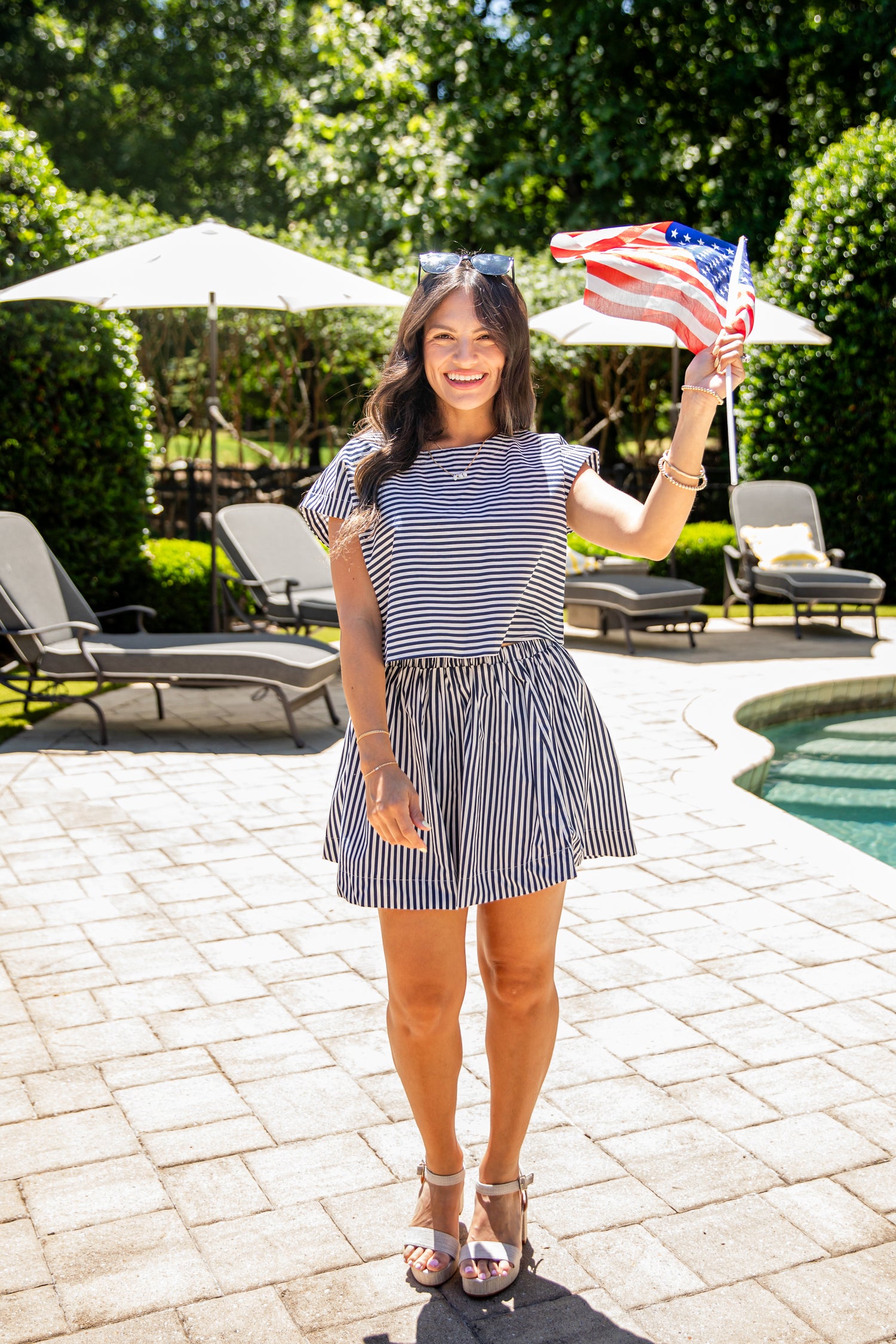 Woman wearing a navy and white striped short-sleeve top paired with a black-and-white striped mini skirt, standing outdoors by a pool on a sunny day