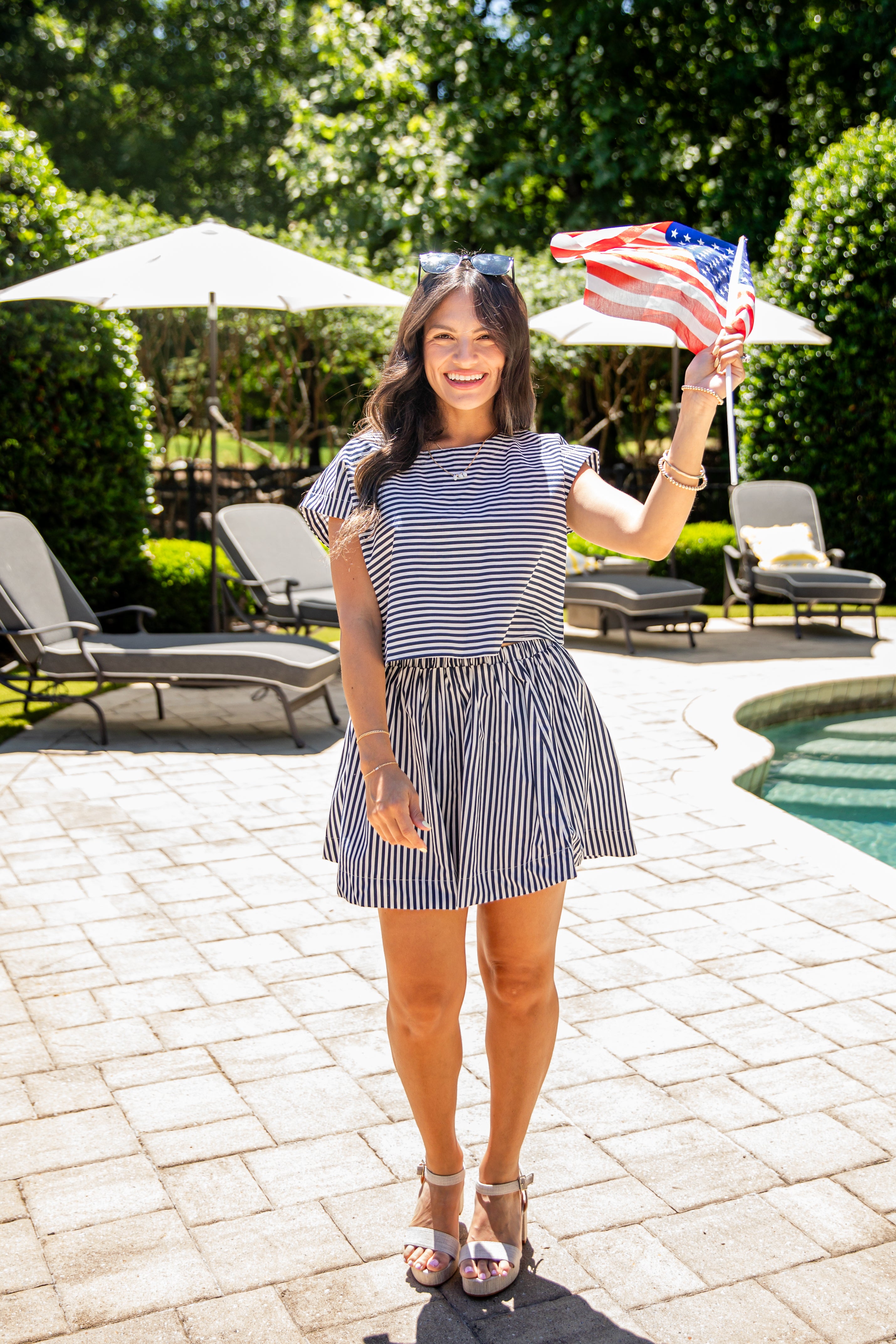 Woman wearing a navy and white striped short-sleeve top paired with a black-and-white striped mini skirt, standing outdoors by a pool on a sunny day